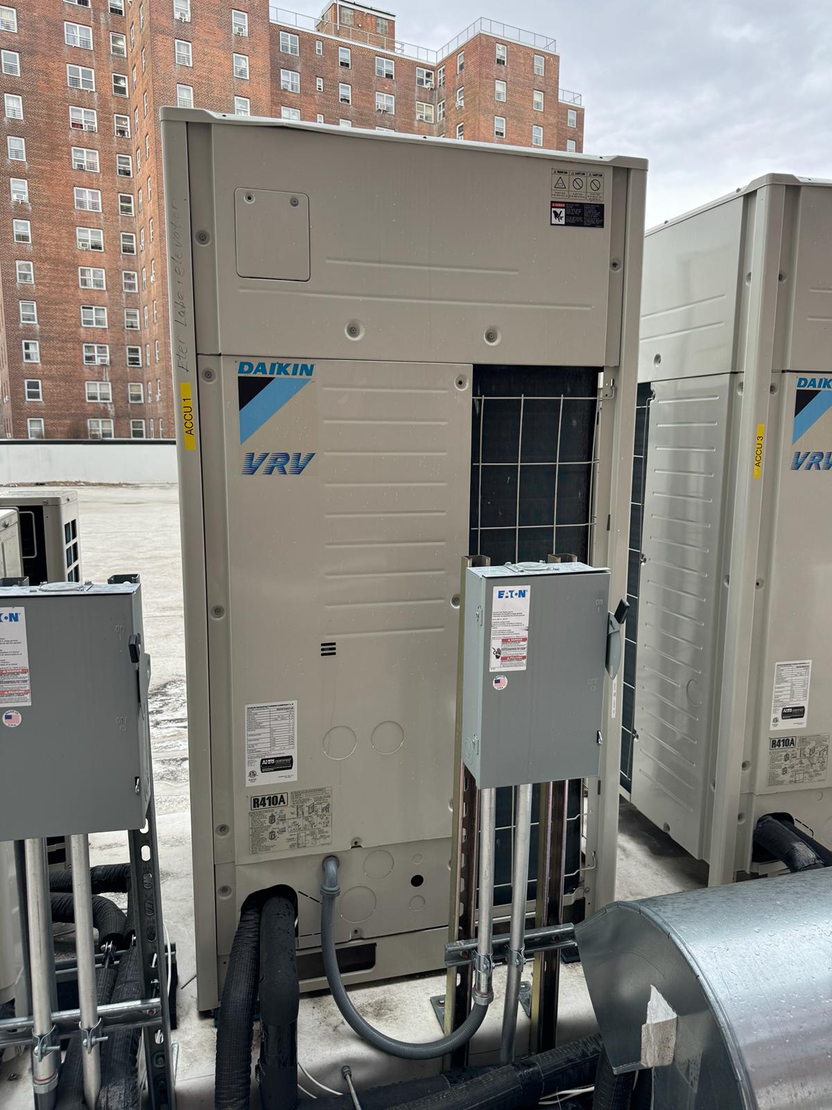 Daikin VRV outdoor units with electrical disconnects and insulated piping beside a brick building