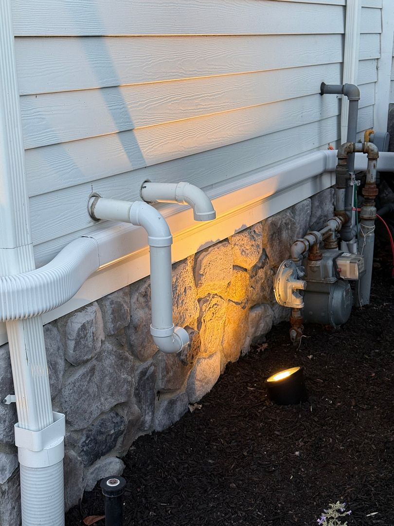 White exterior vent pipes passing through siding above a stone foundation