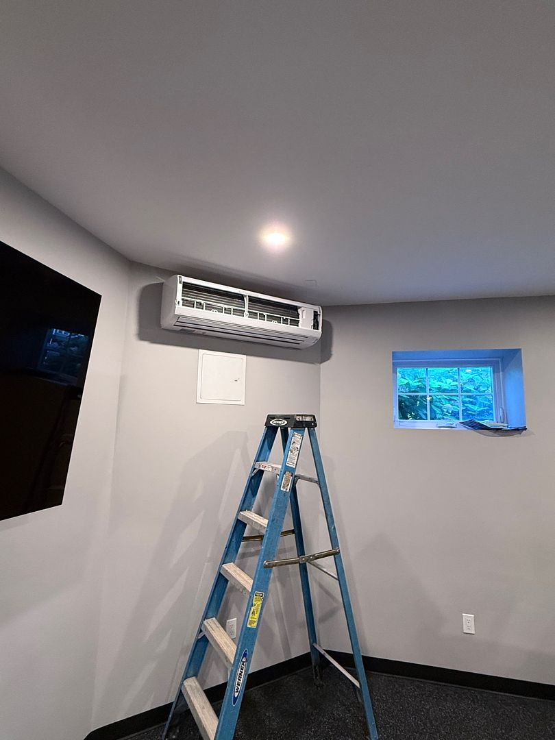 Indoor mini-split with its front cover open above a service ladder