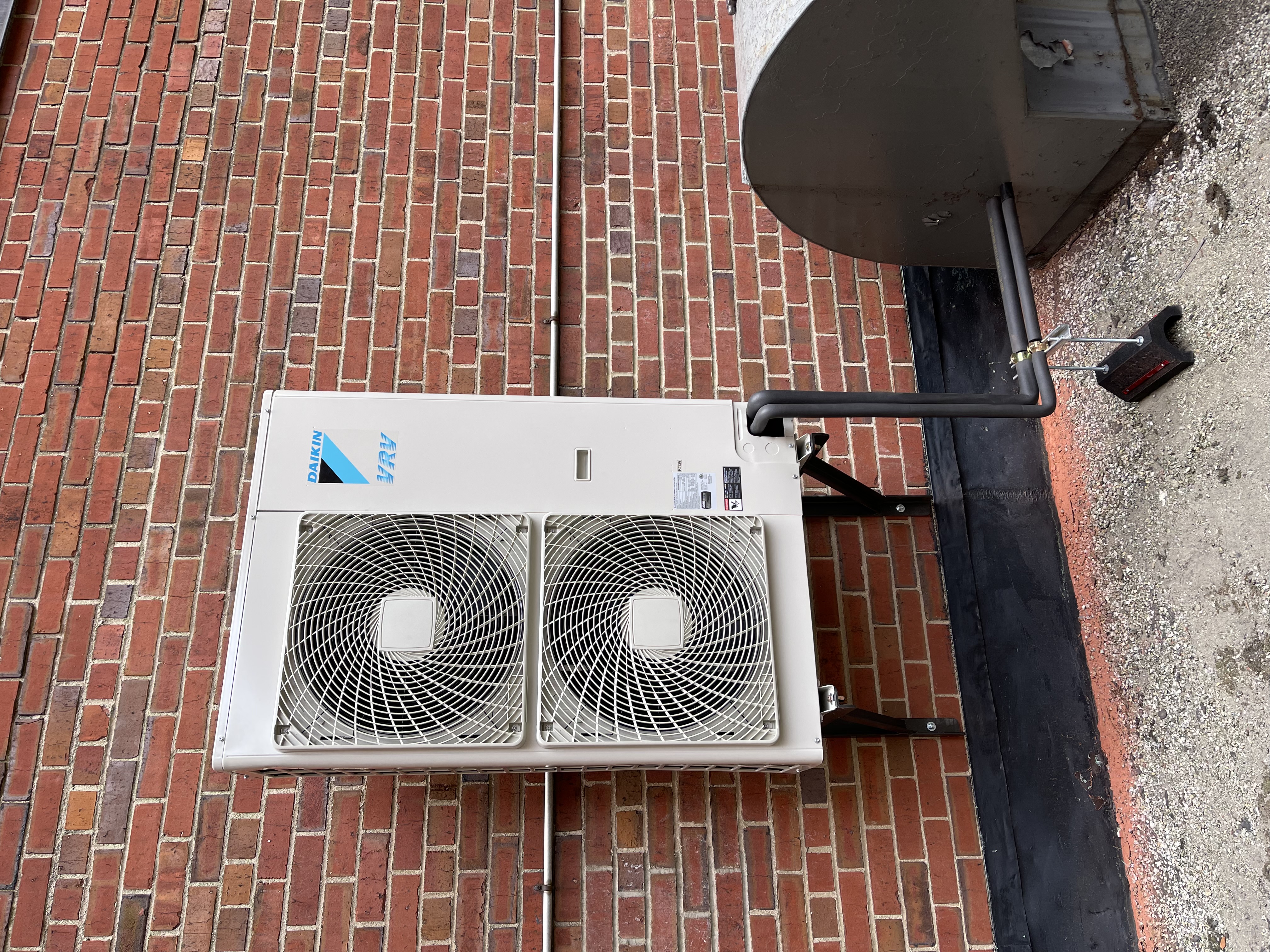 Daikin dual-fan outdoor unit mounted on brackets against a brick wall